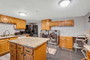 Kitchen with sink, washing machine and dryer, appliances with stainless steel finishes, a kitchen island, and a kitchen bar