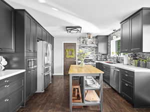 Kitchen featuring stainless steel appliances, wall chimney range hood, dark hardwood / wood-style flooring, backsplash, and pendant lighting