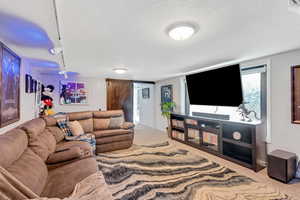 Living room featuring a barn door, rail lighting, light colored carpet, and a textured ceiling