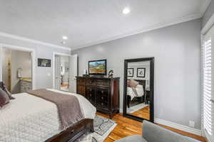 Bedroom with connected bathroom, crown molding, and light hardwood / wood-style floors