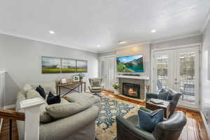 Living room featuring hardwood / wood-style flooring, a tiled fireplace, crown molding, a textured ceiling, and french doors