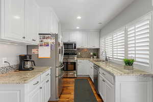 Kitchen with light granite countertops, sink, dark hardwood / wood-style floors, white cabinets, and appliances with stainless steel finishes