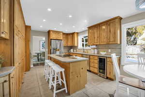 Kitchen featuring a center island, light tile patterned floors, beverage cooler, and appliances with stainless steel finishes