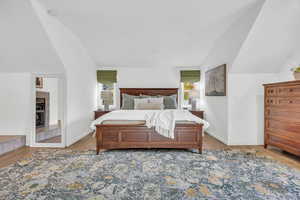 Bedroom with light hardwood / wood-style flooring, multiple windows, and lofted ceiling