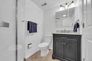 Bathroom with vanity, an enclosed shower, toilet, and tile patterned flooring