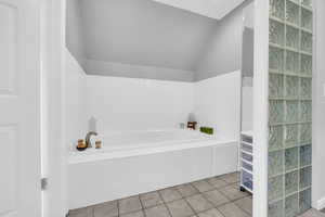 Bathroom with tile patterned floors, lofted ceiling, and tiled tub