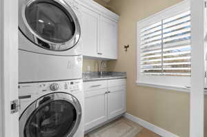 Washroom featuring cabinets, light tile patterned floors, stacked washer and dryer, and sink