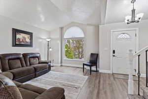 Living room with an inviting chandelier, a textured ceiling, light hardwood / wood-style flooring, and lofted ceiling