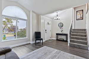 Entrance foyer with dark hardwood / wood-style floors, a textured ceiling, an inviting chandelier, and vaulted ceiling