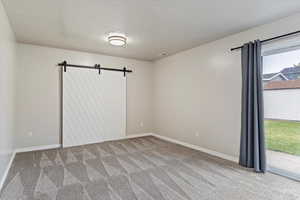 Carpeted spare room with a textured ceiling and a barn door