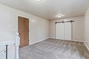 Unfurnished bedroom with a textured ceiling, carpet floors, and a barn door