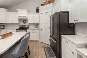 Kitchen featuring white cabinets, a kitchen breakfast bar, vaulted ceiling, light wood-type flooring, and appliances with stainless steel finishes