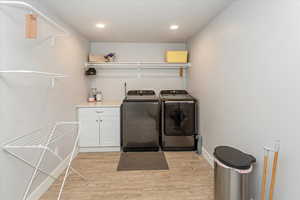 Clothes washing area with independent washer and dryer and light hardwood / wood-style flooring