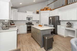 Kitchen with sink, stainless steel appliances, a kitchen island, white cabinets, and light wood-type flooring