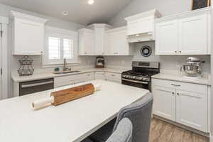 Kitchen with appliances with stainless steel finishes, light wood-type flooring, sink, white cabinetry, and lofted ceiling