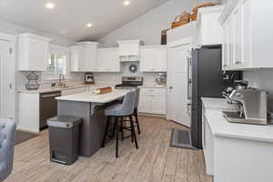 Kitchen featuring white cabinetry, light hardwood / wood-style floors, lofted ceiling, a kitchen island, and appliances with stainless steel finishes