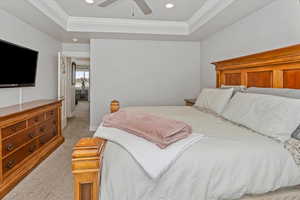 Bedroom featuring ceiling fan, crown molding, light carpet, and a tray ceiling