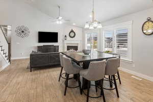 Dining area with ceiling fan with notable chandelier, light wood-type flooring, and vaulted ceiling