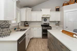 Kitchen with stainless steel appliances, vaulted ceiling, sink, white cabinets, and light hardwood / wood-style floors