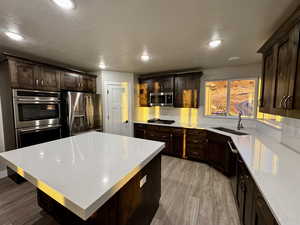 Kitchen with sink, a center island, stainless steel appliances, light hardwood / wood-style flooring, and dark brown cabinets