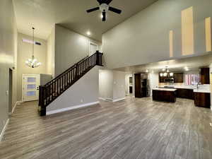 Unfurnished living room featuring ceiling fan with notable chandelier, a towering ceiling, and light hardwood / wood-style flooring