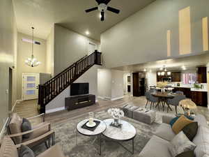 Living room with wood-type flooring, ceiling fan with notable chandelier, and high vaulted ceiling