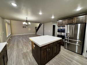 Kitchen featuring dark brown cabinets, a kitchen island, light wood-type flooring, and appliances with stainless steel finishes