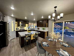 Kitchen with appliances with stainless steel finishes, dark brown cabinets, an inviting chandelier, light hardwood / wood-style floors, and hanging light fixtures