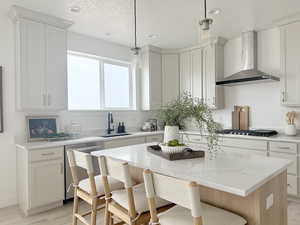 Kitchen featuring stainless steel appliances, hanging light fixtures, a sink, a kitchen island, and wall chimney exhaust hood