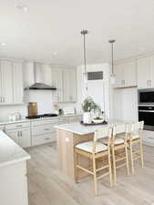 Kitchen featuring stainless steel appliances, a kitchen island, hanging light fixtures, wall chimney range hood, and light stone countertops