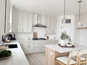 Kitchen with wall chimney exhaust hood, stainless steel gas stovetop, hanging light fixtures, light stone countertops, and a kitchen breakfast bar