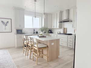 Kitchen with stainless steel gas cooktop, a kitchen island, light countertops, wall chimney range hood, and a kitchen bar