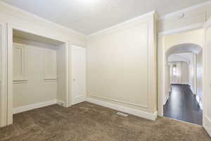 Spare room featuring dark colored carpet, a textured ceiling, and crown molding