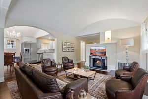 Living room with dark hardwood / wood-style floors, an inviting chandelier, lofted ceiling, and sink (Staged by AI)