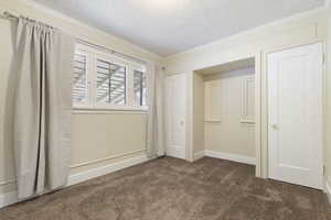 Unfurnished bedroom featuring dark carpet, crown molding, and a textured ceiling