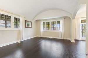 Unfurnished room featuring a textured ceiling, lofted ceiling, and dark wood-type flooring