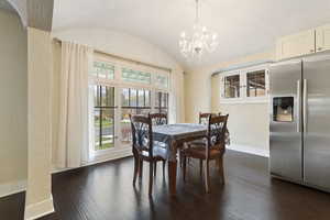 Dining space with a notable chandelier, dark hardwood / wood-style floors, a textured ceiling, and vaulted ceiling