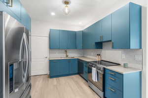 Kitchen with light hardwood / wood-style floors, stainless steel appliances, decorative backsplash, sink, and blue cabinetry