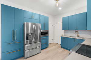 Kitchen with light wood-type flooring, appliances with stainless steel finishes, and blue cabinets