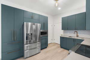 Kitchen featuring tasteful backsplash, light hardwood / wood-style flooring, blue cabinets, and appliances with stainless steel finishes