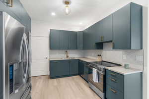 Kitchen featuring appliances with stainless steel finishes, tasteful backsplash, sink, blue cabinetry, and light hardwood / wood-style floors