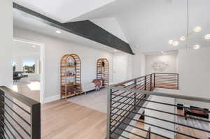 Hall with light hardwood / wood-style floors, vaulted ceiling, and an inviting chandelier