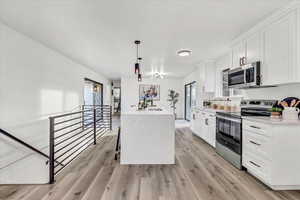 Kitchen with white cabinets, light hardwood / wood-style floors, hanging light fixtures, and appliances with stainless steel finishes