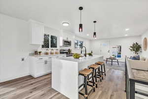 Kitchen with appliances with stainless steel finishes, pendant lighting, a center island with sink, light hardwood / wood-style flooring, and white cabinets