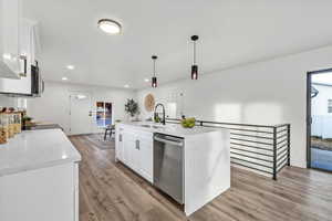 Kitchen featuring light wood-type flooring, white cabinets, dishwasher, hanging light fixtures, and an island with sink