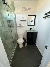 Bathroom featuring tile patterned floors, toilet, an enclosed shower, and vanity