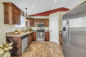 Kitchen with sink, vaulted ceiling, decorative light fixtures, appliances with stainless steel finishes, and light wood-type flooring