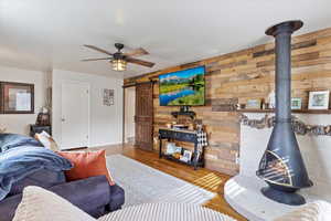 Living room featuring ceiling fan, wooden walls, a barn door, hardwood / wood-style flooring, and a wood stove