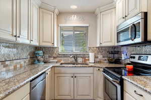 Kitchen featuring decorative backsplash, sink, light stone countertops, and appliances with stainless steel finishes