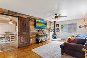 Living room with a barn door, hardwood / wood-style flooring, ceiling fan, and wood walls